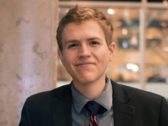 headshot of person wearing gray suit, shirt and tie