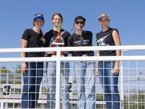 four people standing behind fence, one holding a trophy