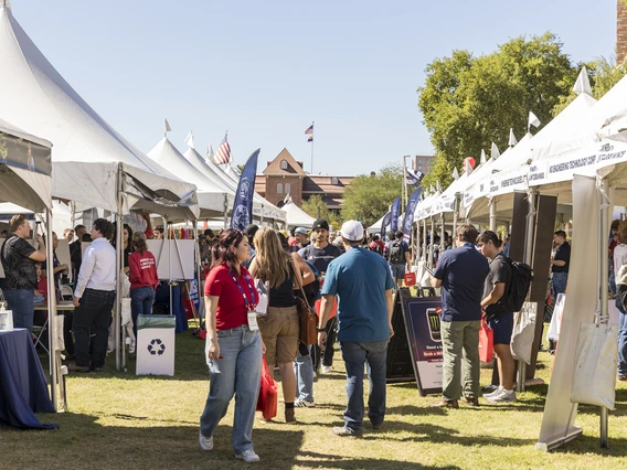 Students walk on a grass lawn botted with white tents.