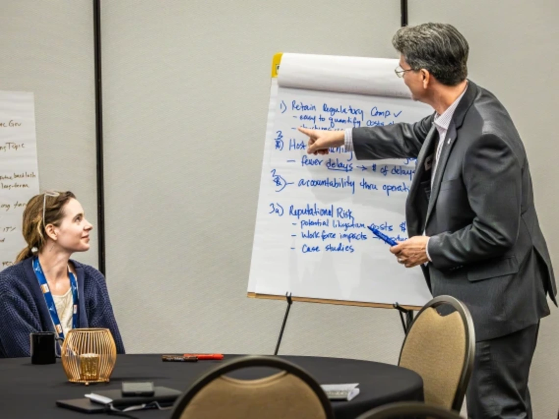 two people, one person standing, point at notes at easel at UA Mining Social License Summit