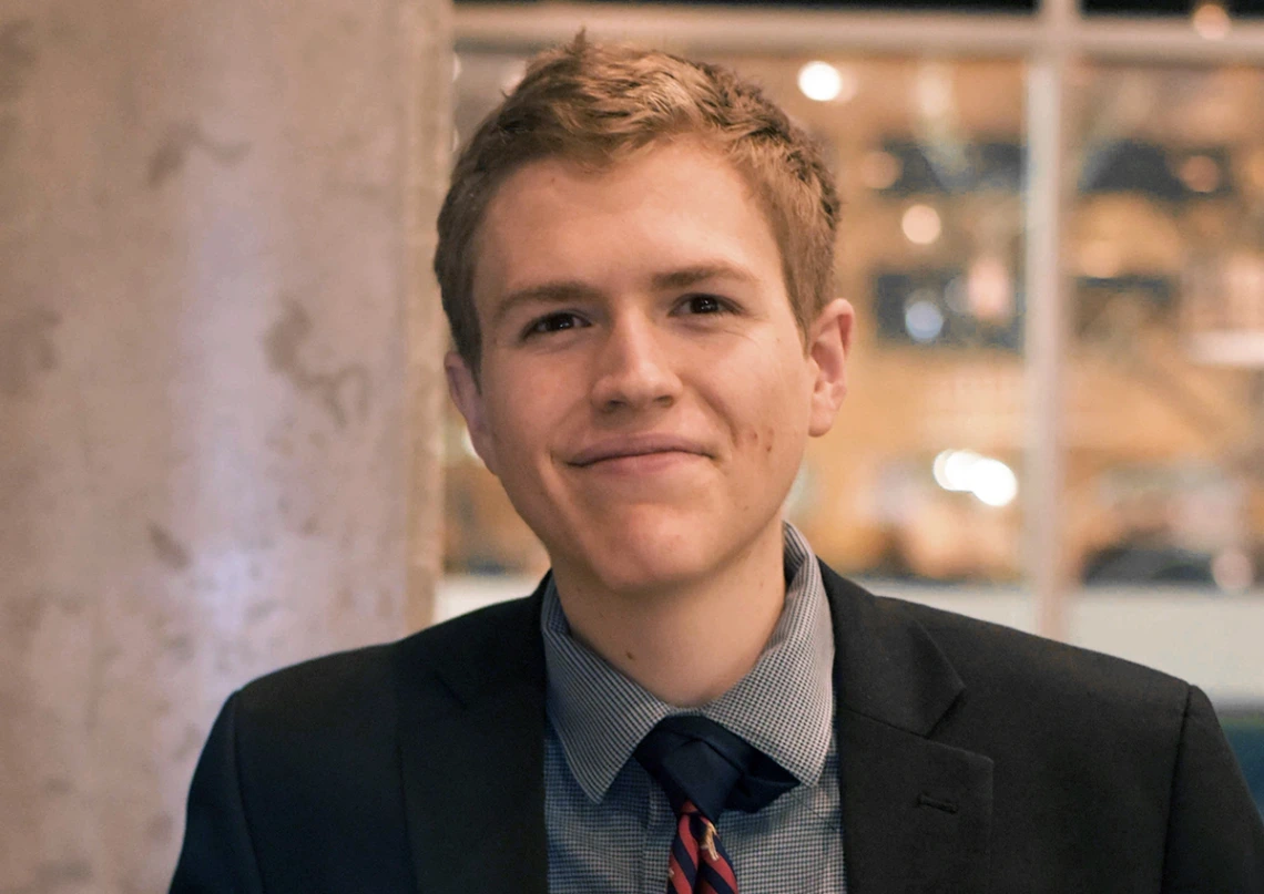 headshot of person wearing gray suit, shirt and tie