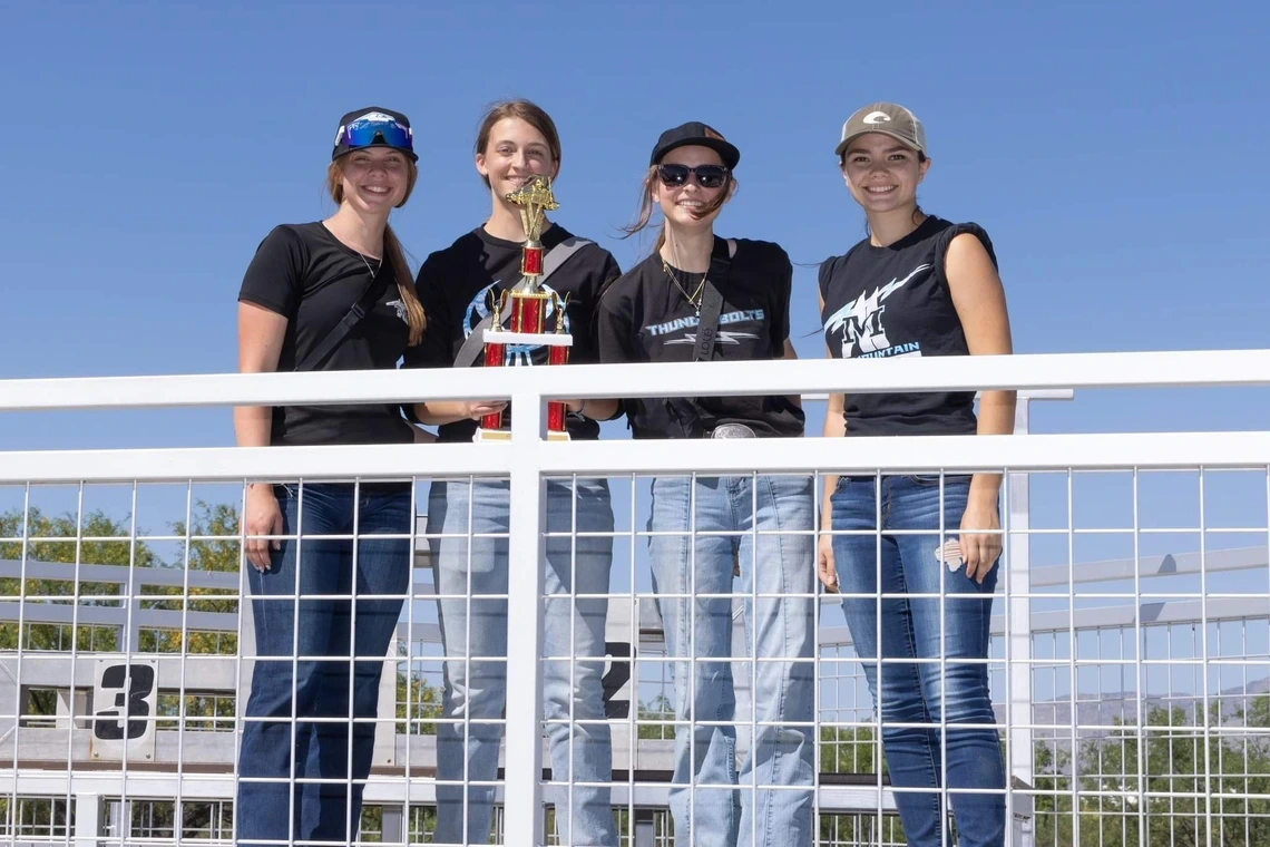 four people standing behind fence, one holding a trophy