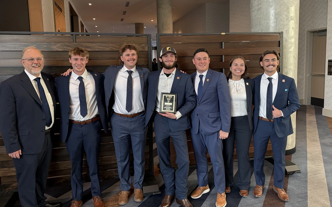 Six men and one woman pose for a photo while wearing dark navy suits.