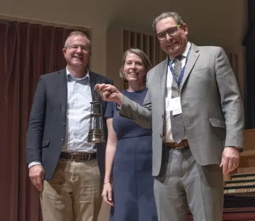 Chalmers holding a mining lantern with Dean Hahn and department head Kray Luxbacher